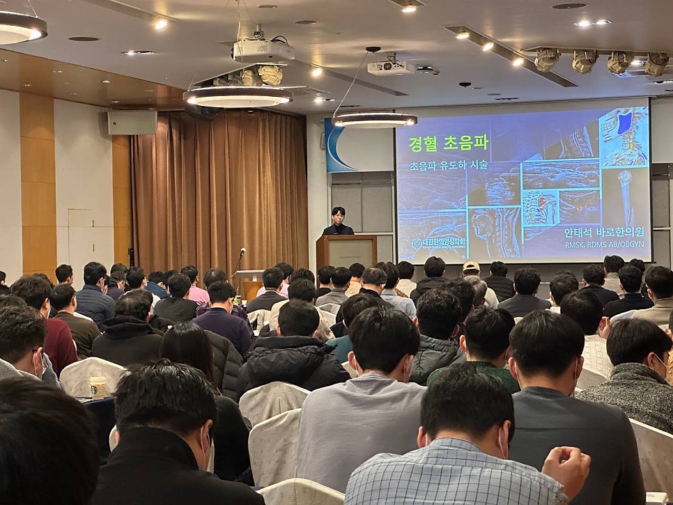 강사가 무대에서 경혈 초음파 관련 내용을 발표하고 있으며, 스크린에는 초음파 사진이 보이고 많은 참석자들이 앉아있다 — 대한한의영상학회 초음파 약침·도침 강의 | 서울 바로한의원