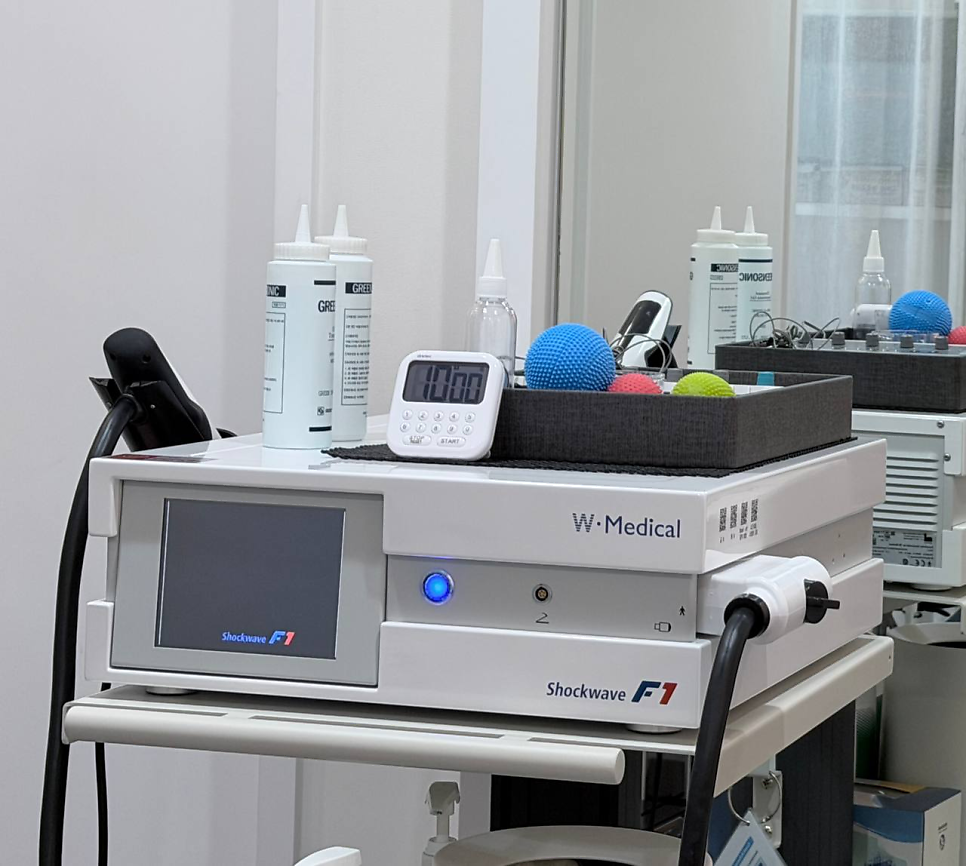 W. Medical Shockwave F1 체외충격파 치료기와 그 위에 놓인 젤, 타이머, 마사지볼 — 서울 바로한의원 초음파 약침·도침