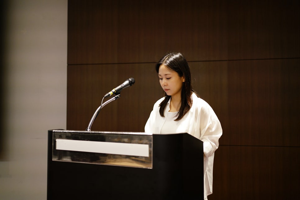 마이크가 있는 검은색 연단 뒤에 서서 아래를 보고 있는 여성 — 대한한의영상학회 초음파 약침·도침 강의 | 서울 바로한의원 문지현 원장