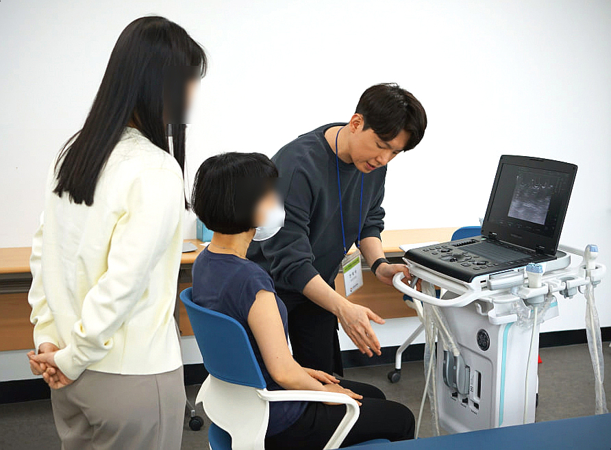 한 남성이 앉아있는 여성에게 초음파 진단기기 사용법을 설명하고 있으며, 다른 여성이 옆에서 교육을 참관하고 있다. 기기 화면에는 초음파 영상이 보인다 — 초음파 정밀 진단 | 서울 바로한의원 초음파 약침·도침·침도
