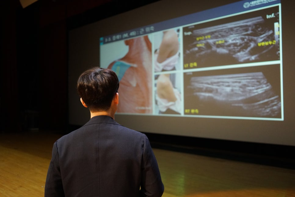 한 사람이 강당에서 스크린을 보며 경혈 초음파 관련 강의를 듣고 있다 — 대한한의영상학회 초음파 약침·도침 강의 | 서울 바로한의원