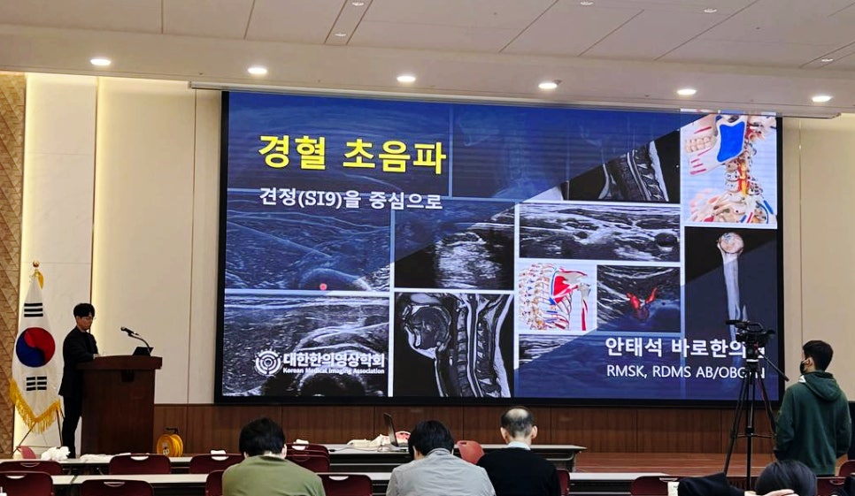 강당에서 한의사가 '경혈 초음파'를 주제로 발표하고 있으며, 스크린에는 초음파 영상과 해부학적 그림 등 다양한 의료 영상이 표시되어 있다 — 대한한의영상학회 초음파 약침·도침 강의 | 서울 바로한의원