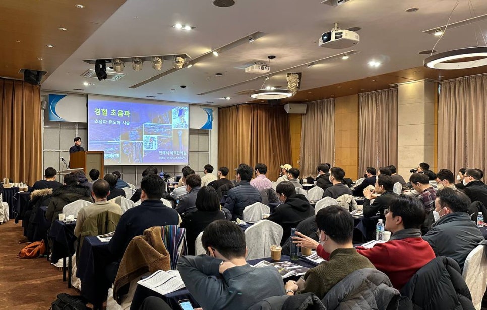 강사가 연단에서 경혈 초음파 관련 내용을 발표하고, 참석자들이 앉아서 듣고 있는 강의실 풍경 — 대한한의영상학회 초음파 약침·도침 강의 | 서울 바로한의원