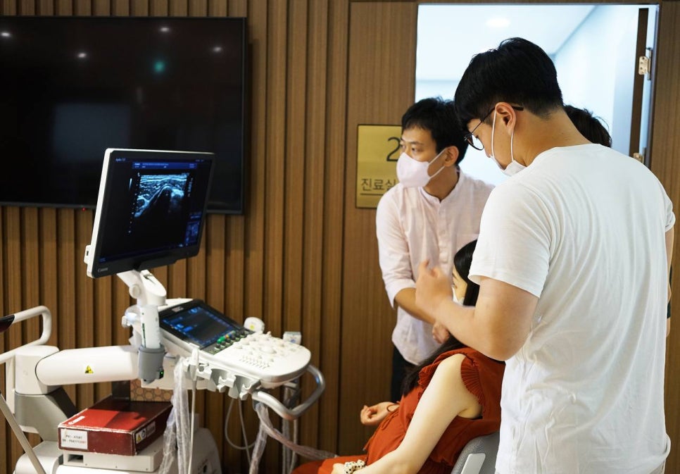 한의원 진료실에서 두 남성이 여성의 팔에 초음파 기기를 사용하며 화면을 보고 있는 모습 — 초음파 정밀 진단 | 서울 바로한의원 초음파 약침·도침·침도