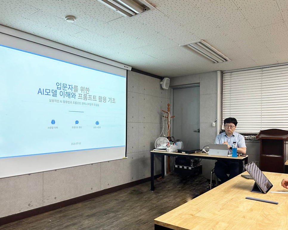 강의실에서 한 남성이 노트북 앞에 앉아 카메라를 응시하고 있으며, 뒤편 스크린에는 'AI 모델 이해와 프롬프트 활용 기초'라는 제목의 발표 자료가 투사되어 있다 — 대한한의영상학회 초음파 약침·도침 강의 | 서울 바로한의원 안태석 원장