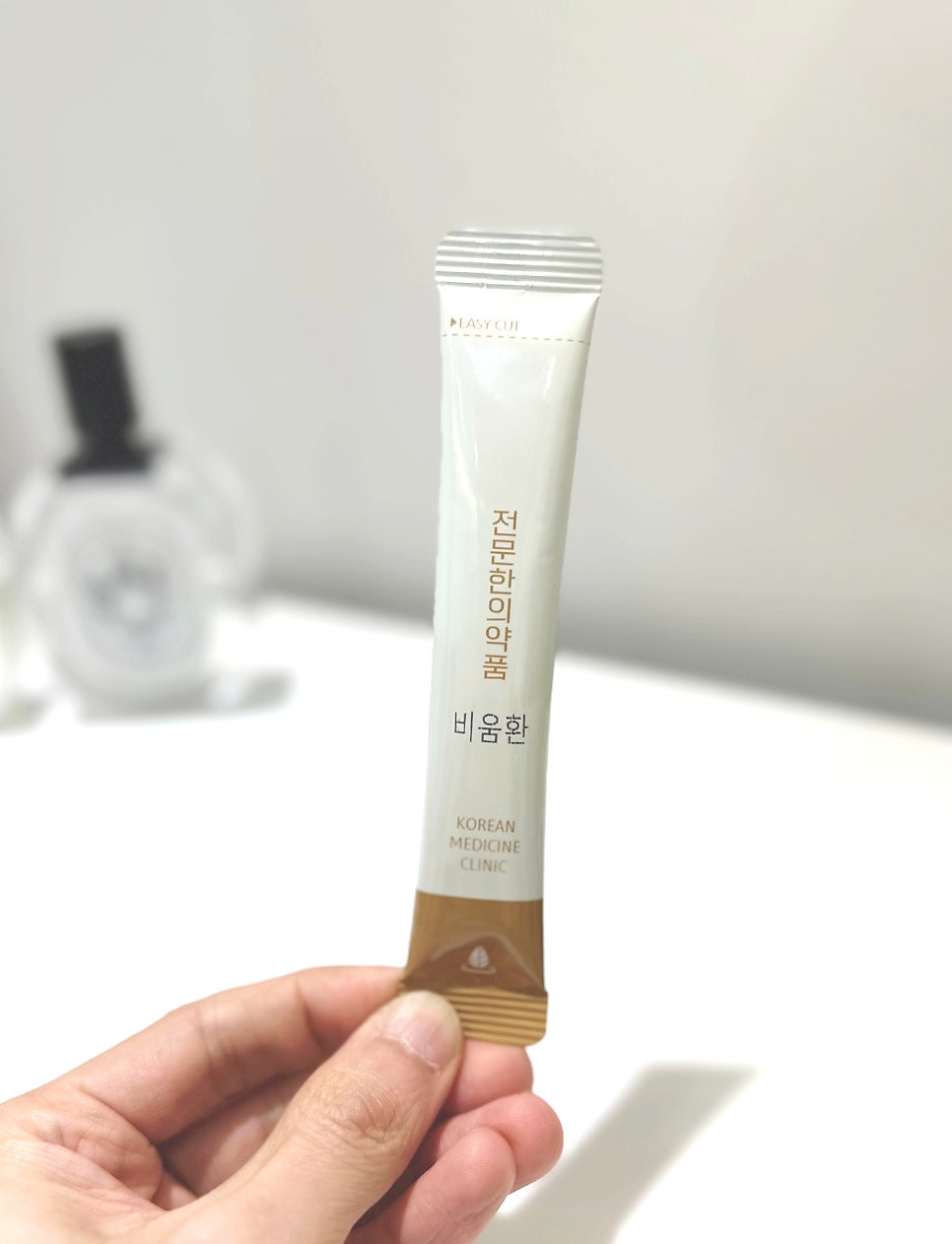 손이 '비움환'이라고 쓰인 흰색과 갈색 스틱형 한약 파우치를 들고 있는 모습 — 서울 바로한의원 초음파 약침·도침
