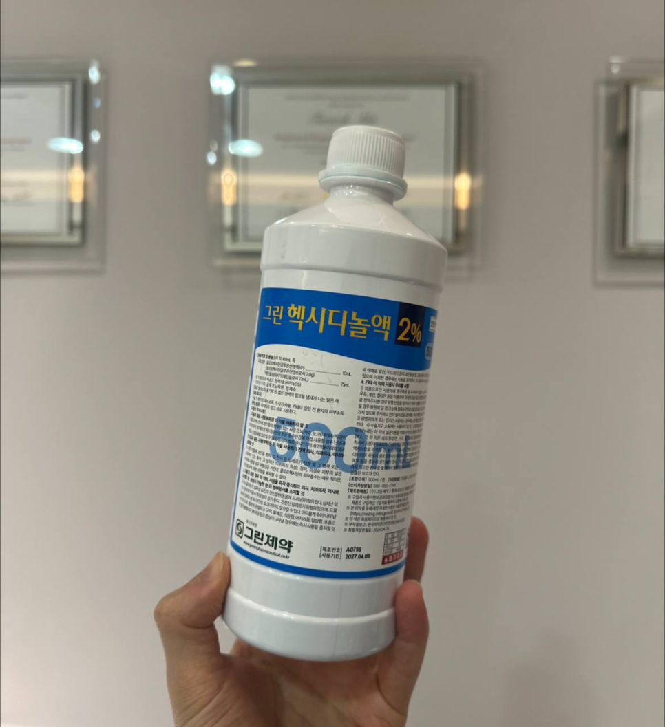 손이 '그린 헥시디놀액 2%'라고 적힌 500ml 흰색 소독약 병을 들고 있습니다 — 서울 바로한의원 초음파 약침·도침