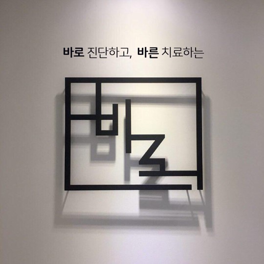 흰 벽에 '바로 진단하고, 바른 치료하는'이라는 검은색 글씨와 검은색 선으로 이루어진 사각형 모양의 장식물이 걸려 있다 — 서울 바로한의원 초음파 약침·도침
