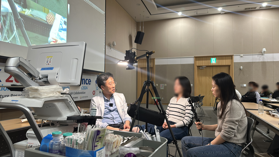 한의사가 초음파 기기 옆에서 인터뷰하고 있으며, 한 여성이 촬영하고 있다 — 대한한의영상학회 초음파 약침·도침 강의 | 서울 바로한의원 문지현 원장