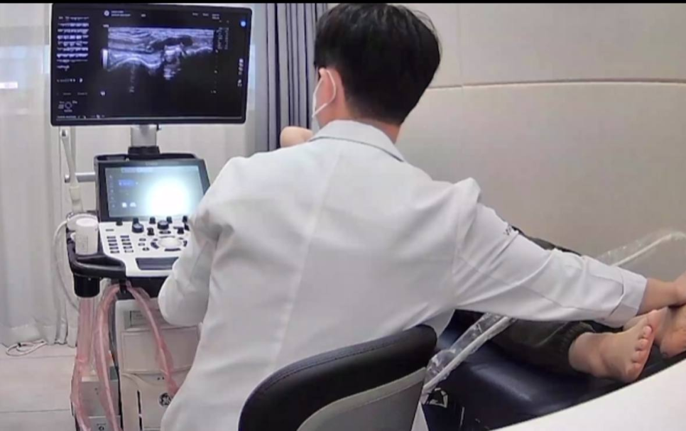 흰색 가운을 입은 의사가 초음파 기기로 환자의 발목을 검사하고 있으며, 모니터에 초음파 영상이 보인다 — 초음파 정밀 진단 | 서울 바로한의원 초음파 약침·도침·침도