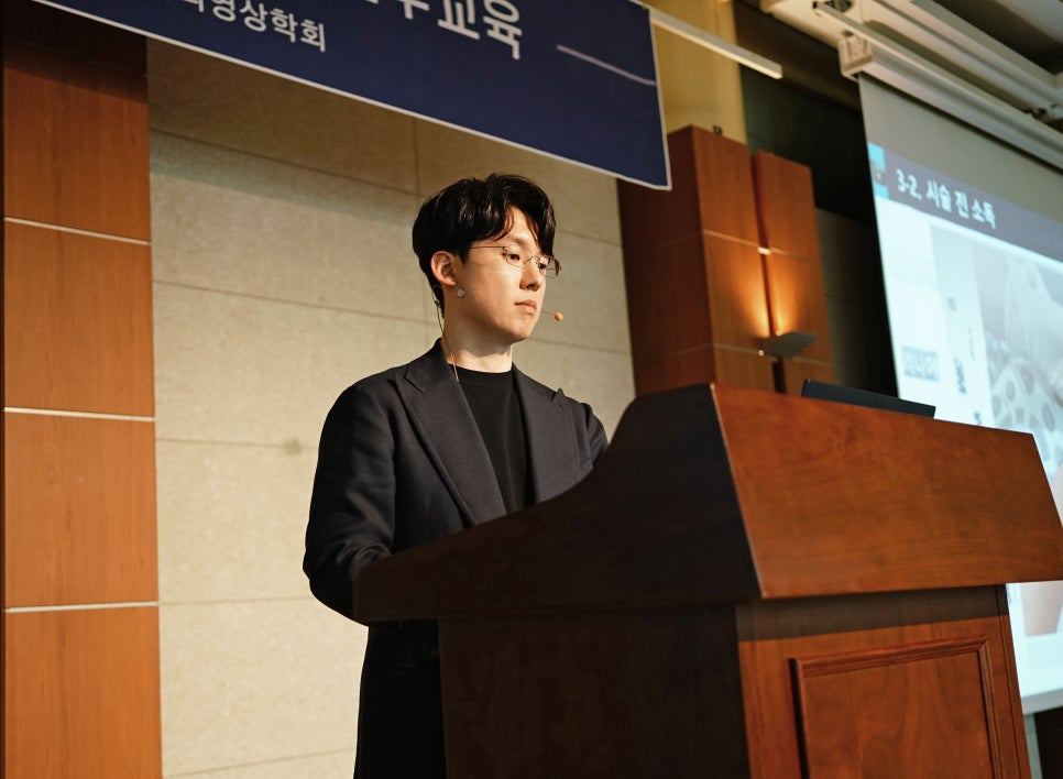 안경을 쓴 남성이 강단에 서서 마이크를 착용하고 강연하고 있으며, 뒤편 스크린에 '시술 전 소독' 문구가 보인다 — 대한한의영상학회 초음파 약침·도침 강의 | 서울 바로한의원 안태석 원장
