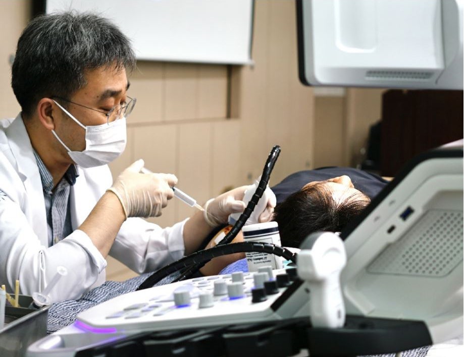 마스크와 장갑을 착용한 한의사가 누워있는 환자에게 초음파 기기를 활용하여 주사 시술을 하고 있다 — 초음파 유도하 약침 시술 | 서울 바로한의원