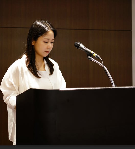 흰색 셔츠를 입은 여성이 마이크가 놓인 검은색 연단 뒤에 서서 아래를 보고 있다 — 대한한의영상학회 초음파 약침·도침 강의 | 서울 바로한의원 문지현 원장