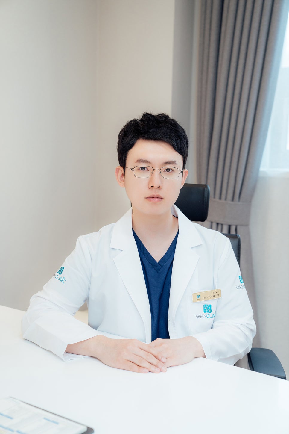 흰색 가운과 안경을 착용한 남자 한의사가 책상에 앉아 카메라를 바라보고 있다 — 서울 바로한의원 초음파 약침·도침