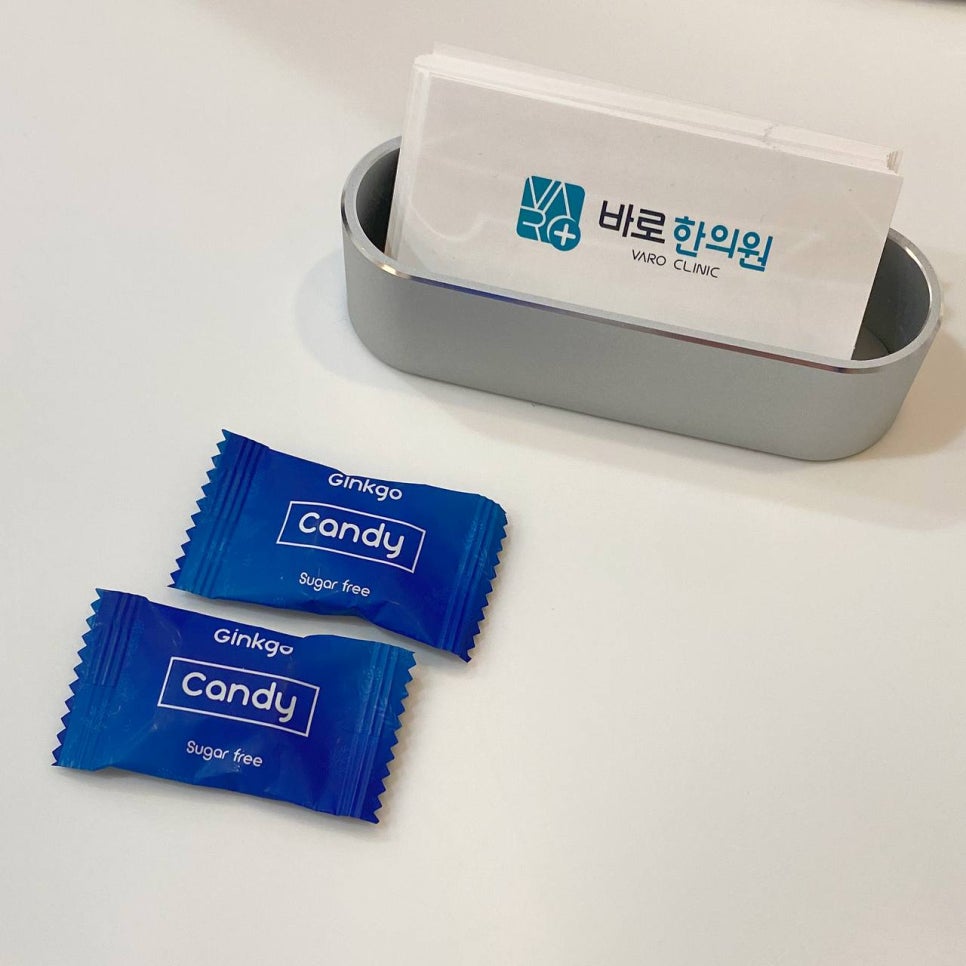 흰색 테이블 위에 파란색 징코 캔디 두 개와 바로 한의원 명함꽂이가 놓여 있다 — 서울 바로한의원 초음파 약침·도침