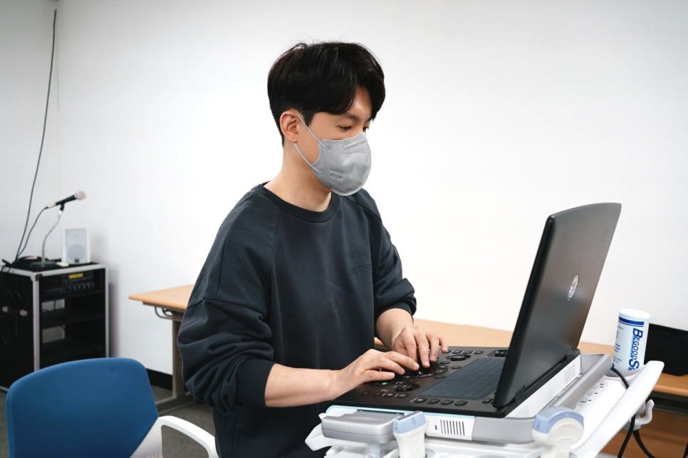 마스크를 쓴 사람이 학술대회에서 초음파 기기를 조작하는 모습 — 초음파 정밀 진단 | 서울 바로한의원 초음파 약침·도침·침도