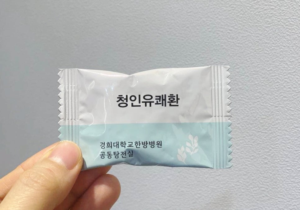 손이 '청인유쾌환'과 '경희대학교한방병원 공동탕전실'이라고 적힌 흰색과 하늘색 포장지를 들고 있는 모습 — 서울 바로한의원 초음파 약침·도침