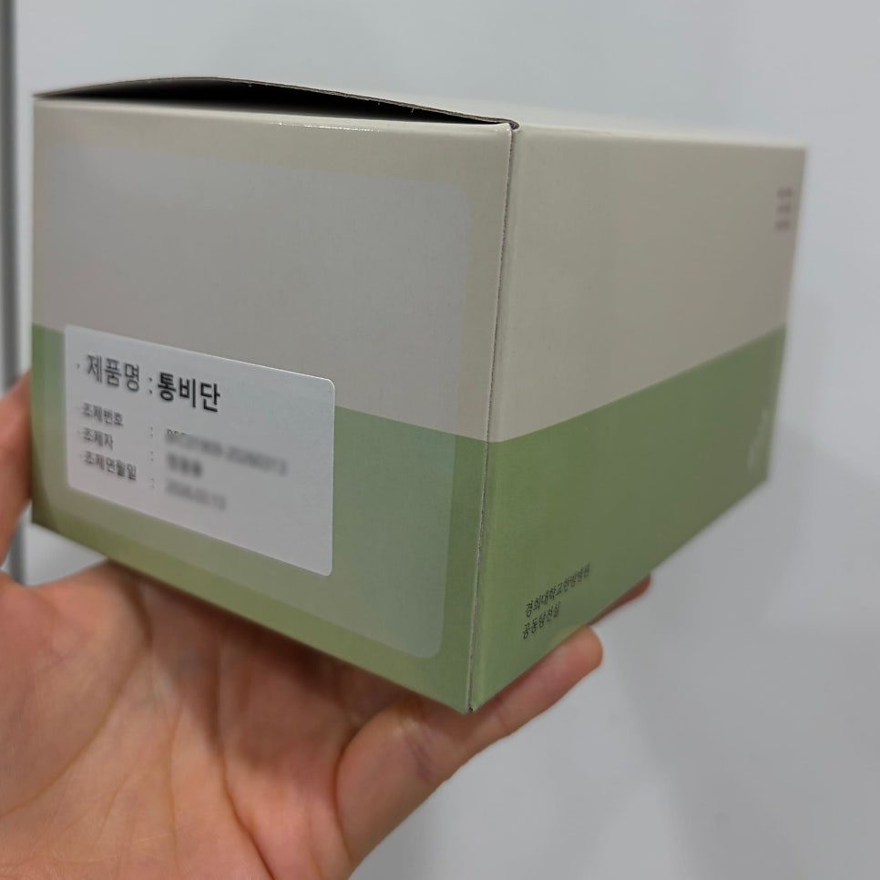 손이 '제품명: 통비단'이라고 적힌 라벨이 붙은 연두색과 베이지색 상자를 들고 있는 모습 — 서울 바로한의원 초음파 약침·도침