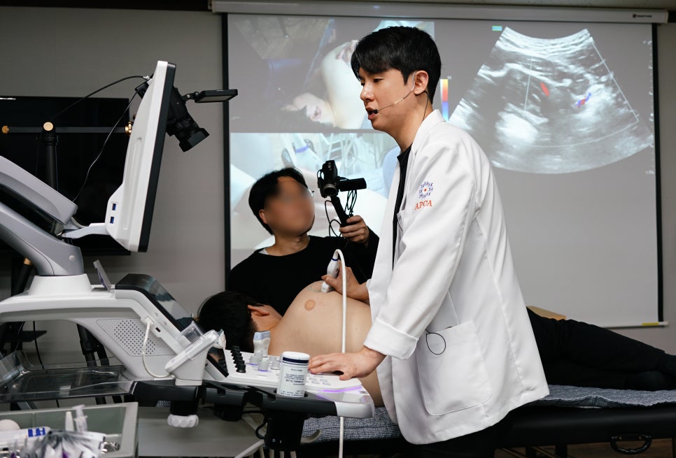 한의사가 환자에게 초음파 검사를 시연하고 있으며, 뒤편 스크린에 초음파 영상이 표시되어 있다 — 초음파 정밀 진단 | 서울 바로한의원 초음파 약침·도침·침도