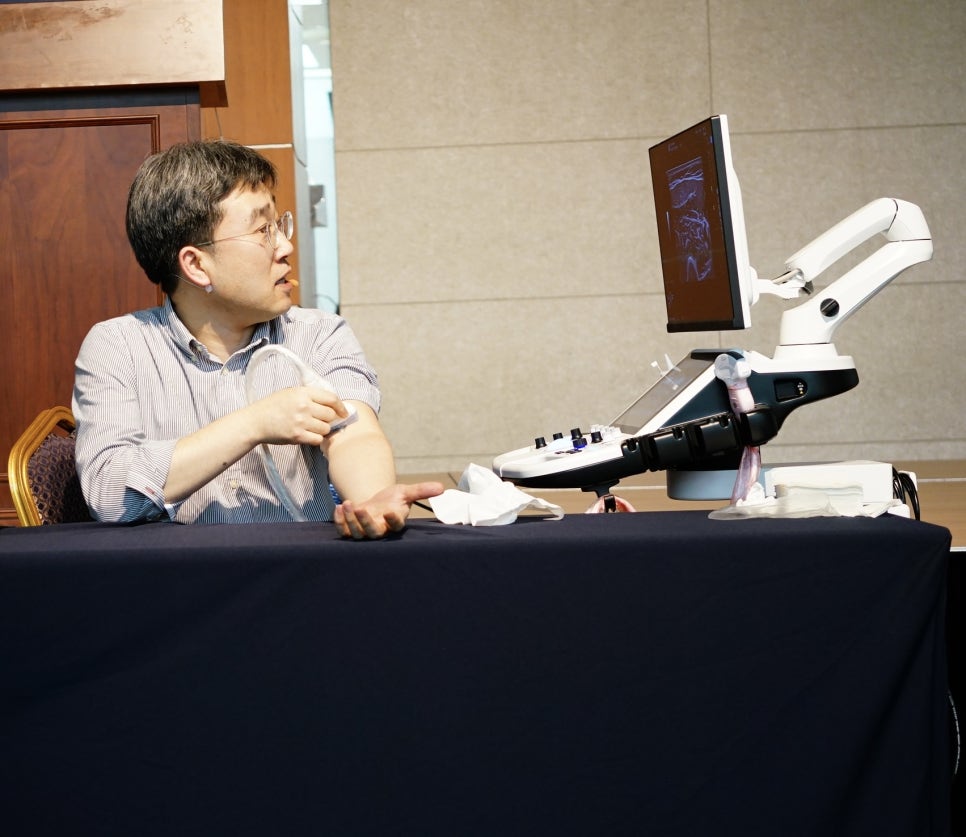 한 남성이 팔에 초음파 기기를 대고 있으며, 옆에 있는 초음파 기기 화면에 영상이 보인다 — 초음파 정밀 진단 | 서울 바로한의원 초음파 약침·도침·침도