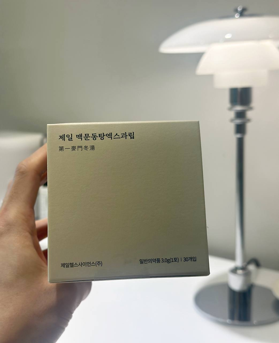 손이 '제일 맥문동탕엑스과립'이라고 적힌 연갈색 상자를 들고 있고, 배경에는 흰색 스탠드 조명이 보인다 — 서울 바로한의원 초음파 약침·도침