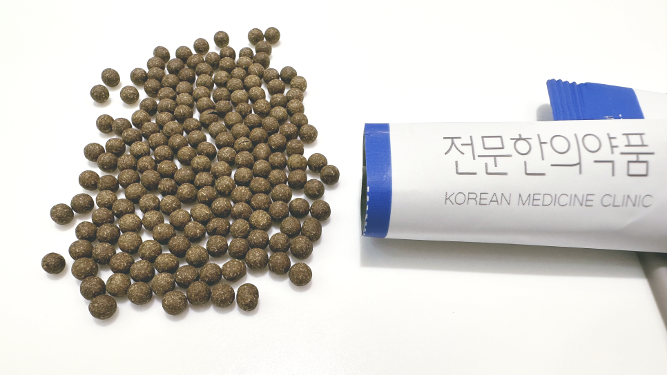흰색 배경에 어두운 갈색 환약들이 흩어져 있고, '전문한의약품'이라고 쓰인 흰색 포장지가 옆에 있습니다 — 서울 바로한의원 초음파 약침·도침