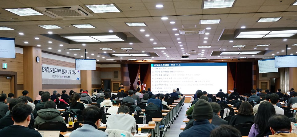 강당에서 많은 사람들이 강연을 듣고 있으며, 전면 스크린에는 아킬레스건병증 한의 치료에 대한 내용이 표시되어 있다 — 대한한의영상학회 초음파 약침·도침 강의 | 서울 바로한의원