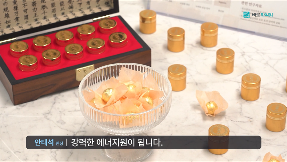 붉은색 안감의 나무 상자에 담긴 금색 용기들과 대리석 위에 놓인 금색 용기들, 그리고 유리 그릇에 담긴 금색 포장 환약들 — 서울 바로한의원 초음파 약침·도침