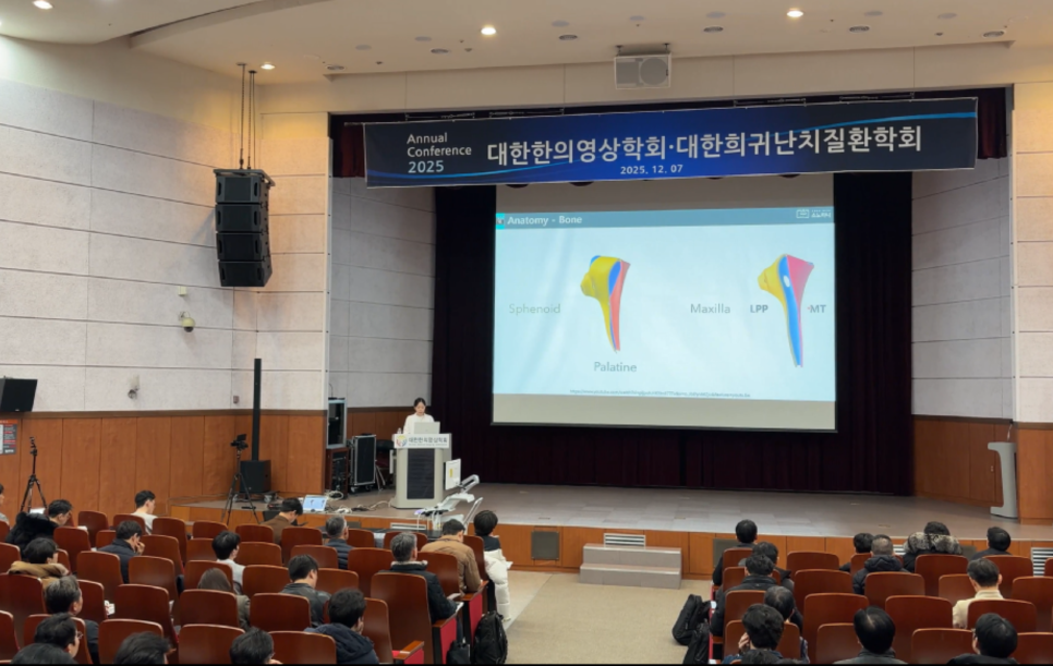 강당에서 강사가 무대 위 스크린에 뼈 해부학 이미지를 띄우고 청중에게 발표하는 모습 — 대한한의영상학회 초음파 약침·도침 강의 | 서울 바로한의원