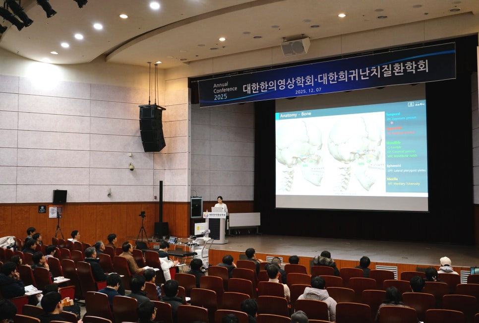강당에서 발표자가 무대 위 스크린에 두개골 해부학 이미지를 띄우고 강연하고 있으며, 청중이 객석에 앉아 경청하고 있다 — 대한한의영상학회 초음파 약침·도침 강의 | 서울 바로한의원