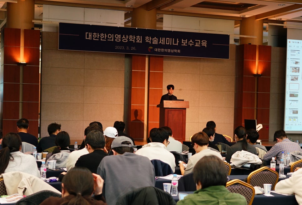 강사가 연단에서 발표하고 여러 참석자가 앉아 경청하는 학술 세미나 풍경 — 대한한의영상학회 초음파 약침·도침 강의 | 서울 바로한의원