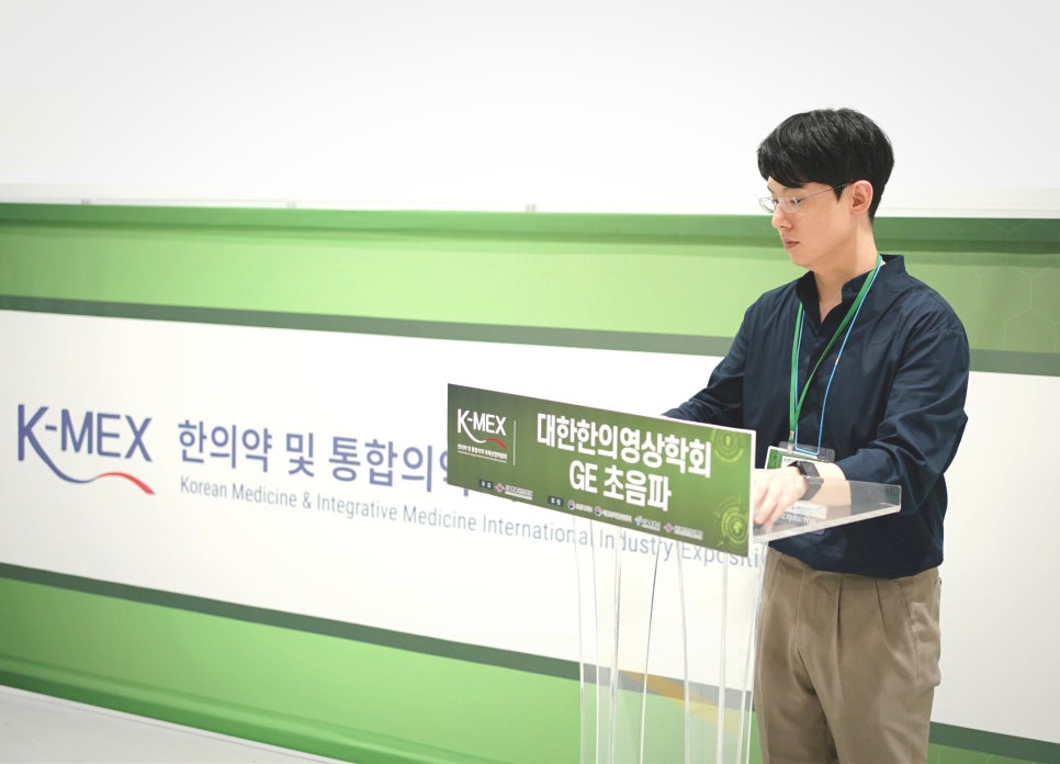 한 남성이 K-MEX 한의학 및 통합의학 배너와 대한한의영상학회 GE 초음파 표지판이 있는 연단에 서 있다 — 대한한의영상학회 초음파 약침·도침 강의 | 서울 바로한의원 안태석 원장