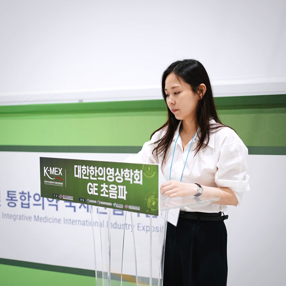 대한한의영상의학회와 GE 초음파 로고가 있는 연단 뒤에 서 있는 여성 — 대한한의영상학회 초음파 약침·도침 강의 | 서울 바로한의원 문지현 원장
