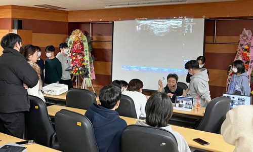 강의실에서 한의대생들이 경혈 초음파 특강을 듣고 있다. 강사가 초음파 기기를 들고 설명하며, 스크린에 초음파 영상이 투사되어 있다 — 대한한의영상학회 초음파 약침·도침 강의 | 서울 바로한의원