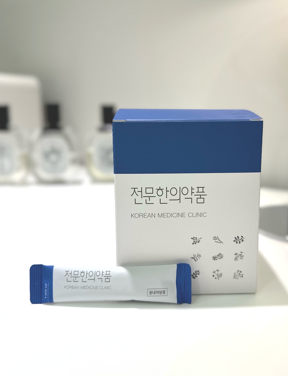흰색과 파란색 상자 하나와 스틱형 파우치 하나가 놓여 있습니다. 상자와 파우치에는 '전문한의약품'과 'KOREAN MEDICINE CLINIC' 문구가 적혀 있으며, 파우치에는 '원내처방용' 문구도 있습니다 — 서울 바로한의원 초음파 약침·도침