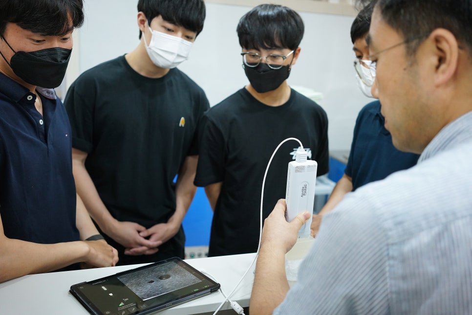 강사가 학생들에게 초음파 기기를 시연하고 있으며, 학생들이 태블릿에 보이는 초음파 영상을 보고 있다 — 초음파 정밀 진단 | 서울 바로한의원 초음파 약침·도침·침도