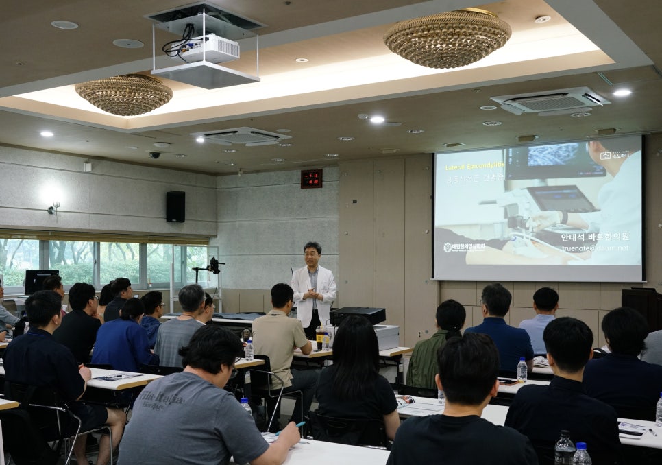 강사가 청중 앞에서 초음파 관련 강좌를 진행하고 있으며, 화면에는 초음파 영상이 보인다 — 대한한의영상학회 초음파 약침·도침 강의 | 서울 바로한의원