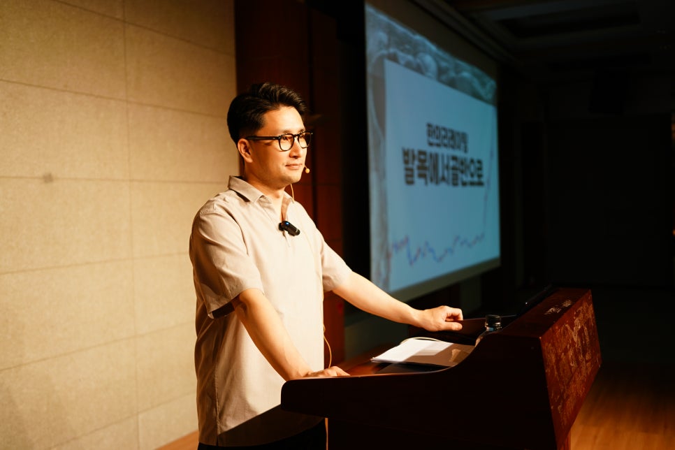 안경을 쓴 남성이 강단에서 마이크를 착용하고 발표하고 있으며, 뒤편 스크린에 글씨가 보인다 — 대한한의영상학회 초음파 약침·도침 강의 | 서울 바로한의원 안태석 원장
