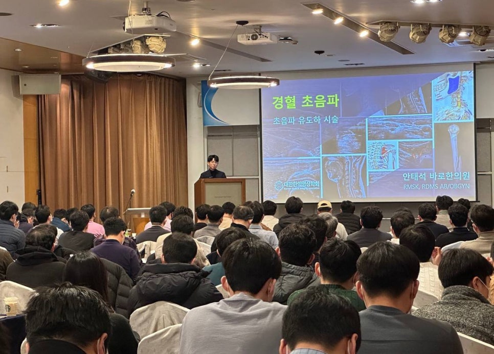 강사가 연단에서 발표하고 있으며, 청중들이 앉아 경혈 초음파 및 초음파 유도 시술 강의를 듣고 있다. 스크린에는 여러 초음파 영상이 표시되어 있다 — 대한한의영상학회 초음파 약침·도침 강의 | 서울 바로한의원