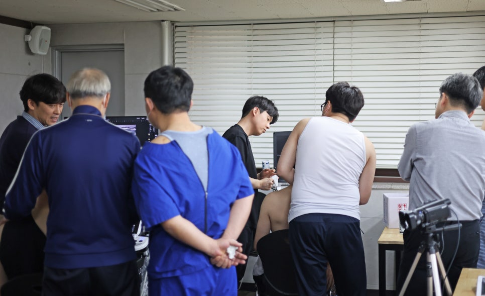 여러 명의 남성들이 모여 초음파 기기를 이용해 어깨를 검사하고 모니터를 보고 있는 모습 — 대한한의영상학회 초음파 약침·도침 강의 | 서울 바로한의원 안태석 원장
