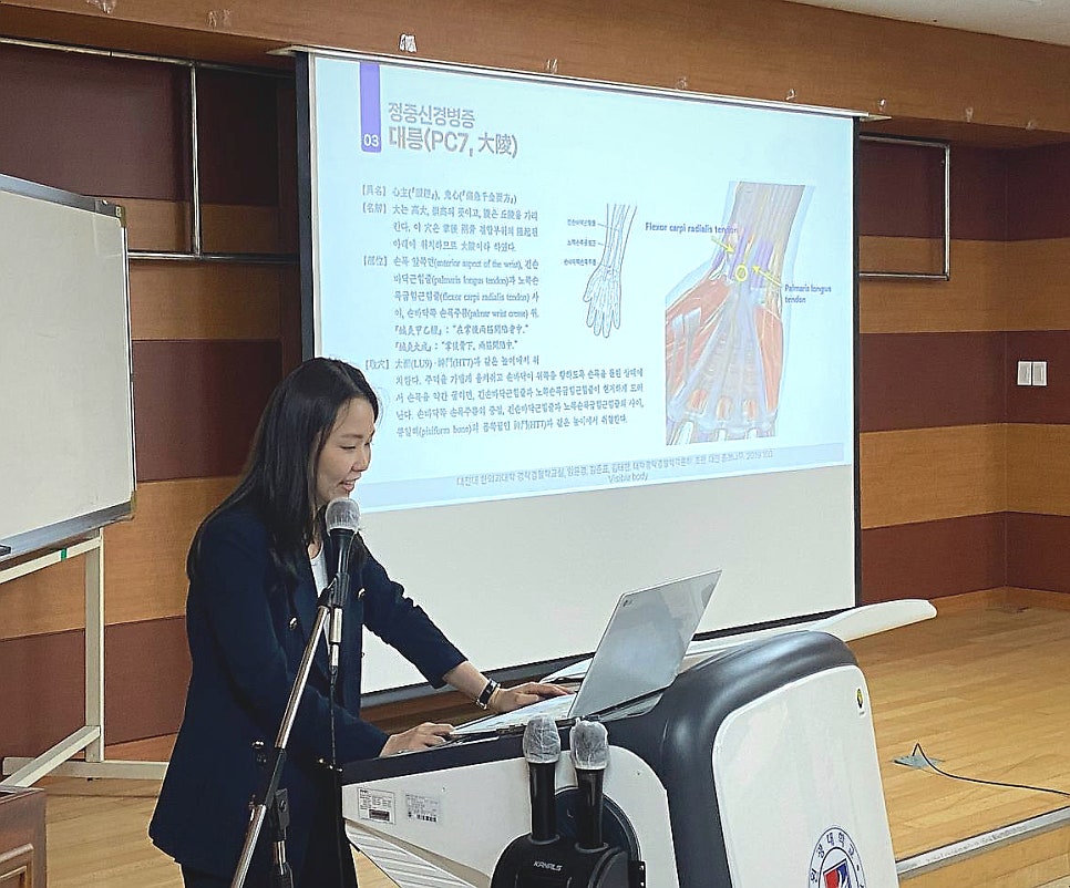 강단에서 한의사가 손목 해부학 슬라이드를 띄우고 강의하는 모습 — 대한한의영상학회 초음파 약침·도침 강의 | 서울 바로한의원
