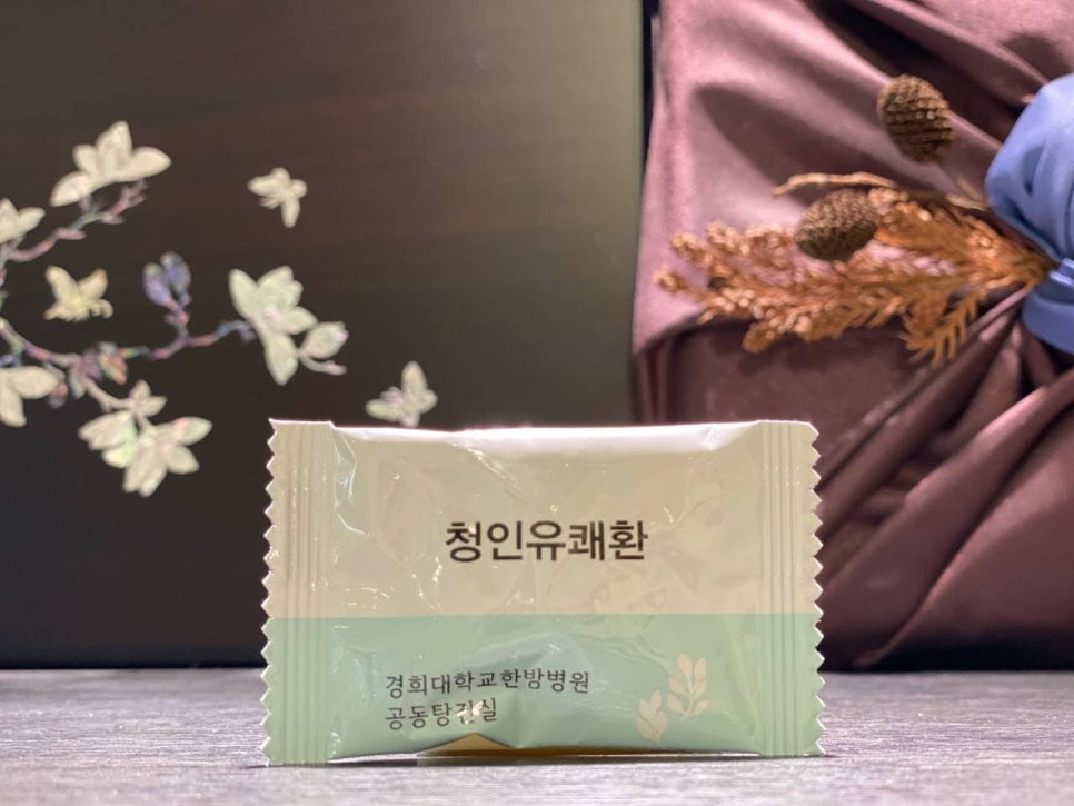 경희대학교한방병원 공동탕전실에서 제조된 청인유쾌환 한 포가 어두운 배경에 놓여 있다 — 서울 바로한의원 초음파 약침·도침