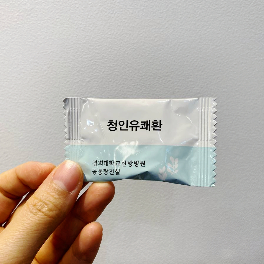 손이 경희대학교 한방병원 공동탕전실의 청인유쾌환이라고 쓰인 흰색과 하늘색 약 포장지를 들고 있는 모습 — 서울 바로한의원 초음파 약침·도침