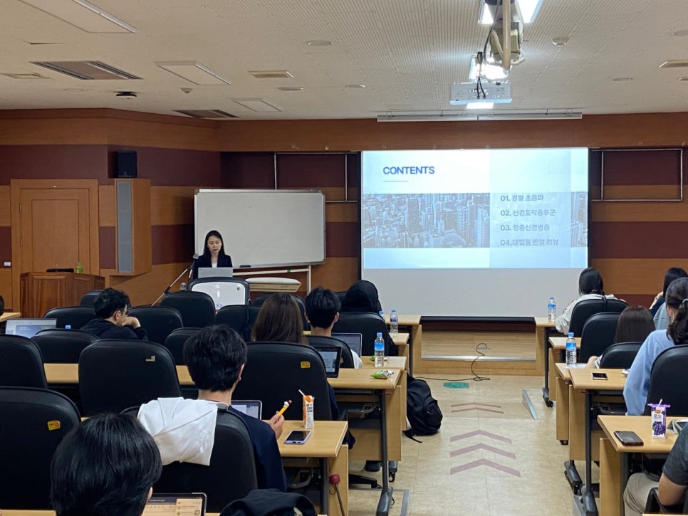 강의실에서 발표자가 강단에 서서 강연하고 있으며, 화면에는 '경혈 초음파'를 포함한 목차가 보인다 — 대한한의영상학회 초음파 약침·도침 강의 | 서울 바로한의원