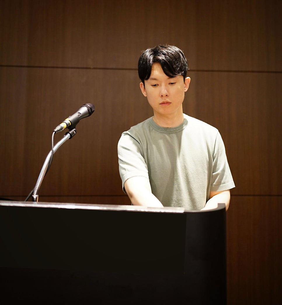 한 남자가 피아노를 연주하고 있으며, 왼쪽에 마이크가 놓여 있다 — 서울 바로한의원 초음파 약침·도침