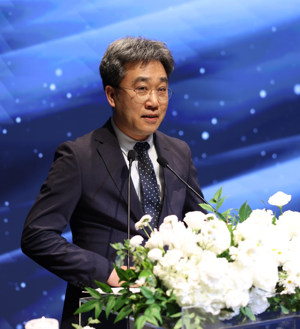 정장과 안경을 착용한 남성이 마이크가 있는 연단에서 발표하고 있으며, 연단 앞에는 흰색 꽃 장식이 놓여 있다 — 대한한의영상학회 초음파 약침·도침 강의 | 서울 바로한의원 안태석 원장