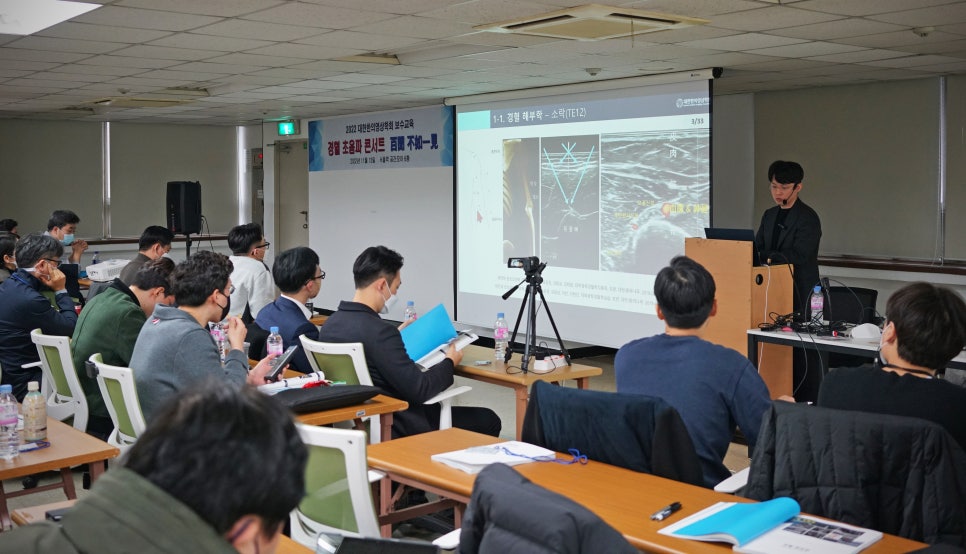 의료 세미나에서 강사가 스크린을 보며 발표하고 참석자들이 앉아서 듣고 있는 모습 — 대한한의영상학회 초음파 약침·도침 강의 | 서울 바로한의원