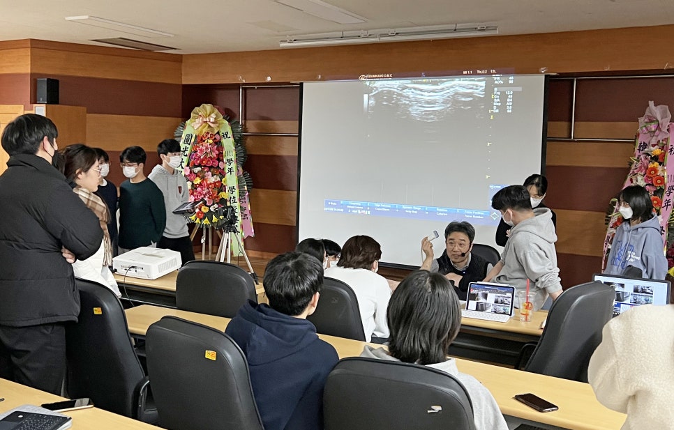 강의실에서 강사가 학생들에게 경혈 초음파 특강을 진행하며 스크린에 초음파 영상이 보이는 모습 — 대한한의영상학회 초음파 약침·도침 강의 | 서울 바로한의원