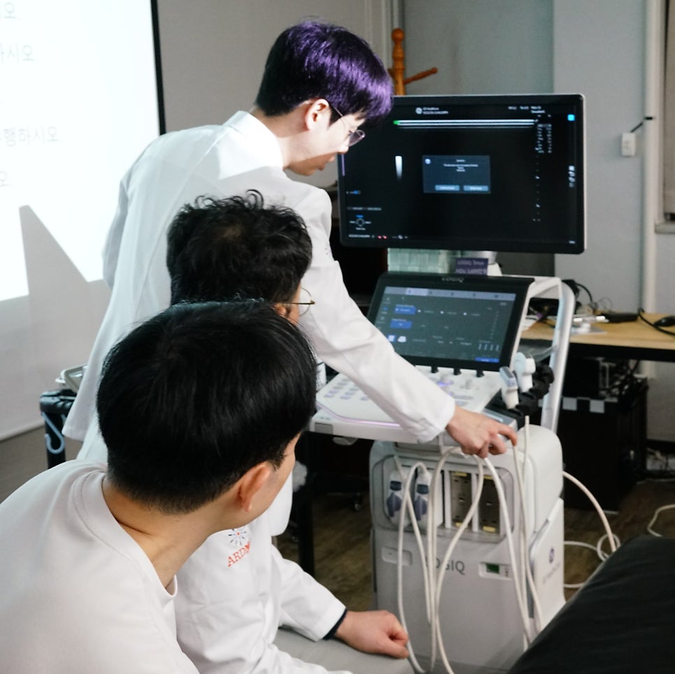 흰색 가운을 입은 한 사람이 초음파 기기를 조작하고 있고, 다른 두 사람이 이를 지켜보고 있는 모습 — 초음파 정밀 진단 | 서울 바로한의원 초음파 약침·도침·침도
