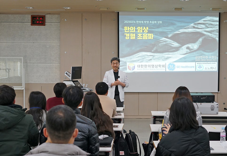 한의사가 강단에서 경혈 초음파 강의를 하고 있으며, 여러 명이 앉아 강의를 듣고 있는 모습 — 대한한의영상학회 초음파 약침·도침 강의 | 서울 바로한의원